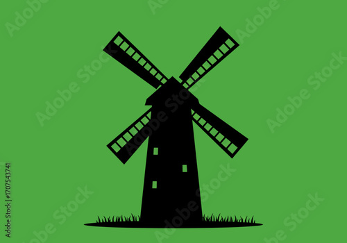 A silhouetted windmill stands against a green background with grass at its base