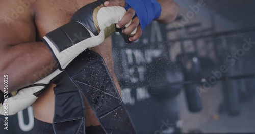 Obraz na plátně Shirtless boxer adjusting blue wrap at boxing gym, with white-gold gloves and pu