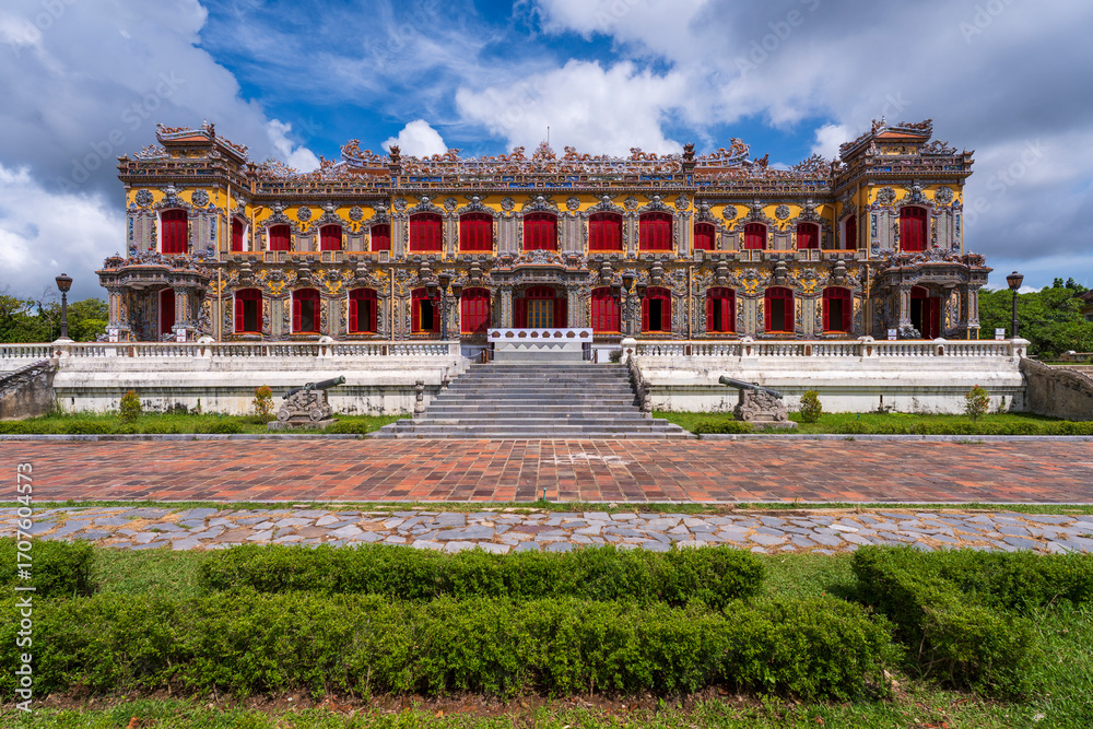 Obraz premium The magnificent, recently restored Kien Trung Palace in Hue, showcasing a vibrant yellow facade, striking red windows, and highly intricate architectural details under a cloudy sky.
