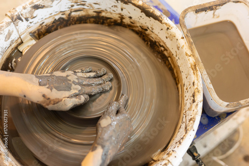 Top view of female hands shaping clay on pottery wheel in selective focus. Artistic handmade ceramic, learning pottery craft, creative process, traditional artisan skill, hobby and craftsmanship.