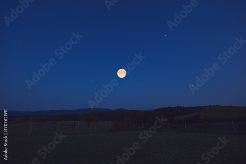 Full Moon with stars, planets and rural countryside tree silhouettes.