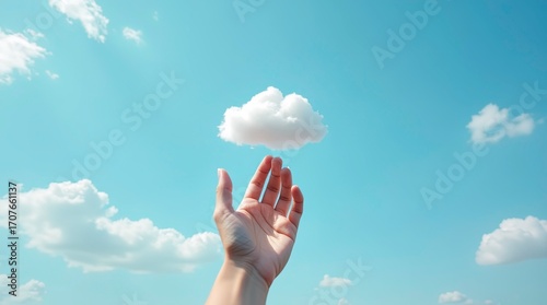 Hand reaching up to hold a fluffy white cloud against a bright blue sky, symbolizing imagination, freedom, and the beauty of dreams, ideal for inspirational and creative concept