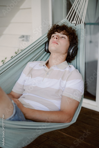 Cuadro en lienzo A young person rests in a hammock wearing headphones, soaking up the sun on a warm summer day