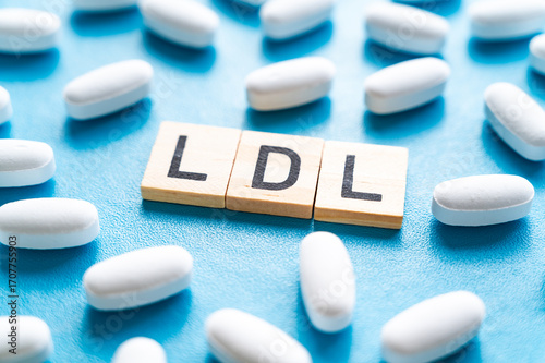 Concept of the difference between HDL and LDL cholesterol, words composed with wooden alphabet on a blue background, and drug tablets surrounding them; bad LDL cholesterol.