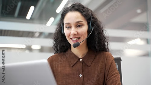 Female corporate operator in wireless headset working in customer support service on helpline telesale talking using laptop sitting in business office. Agent of call center advises client. Close up