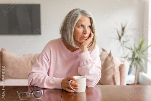 Sad pensive middle age woman looking down depressed sitting on the sofa