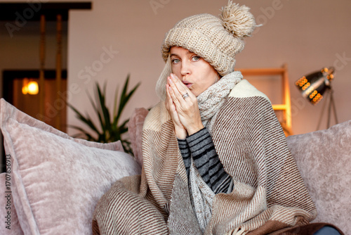 Cuadro en lienzo Woman warmly clothed and hat in a cold home sitting on couch