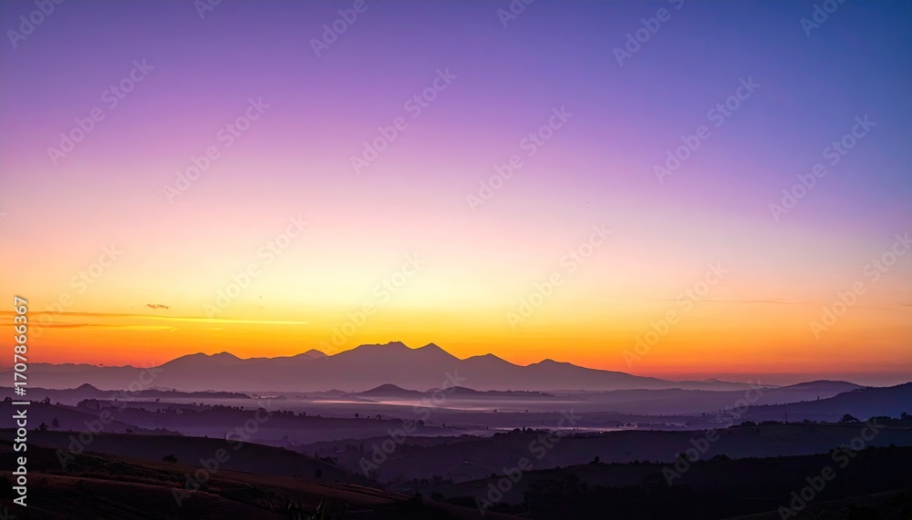 Obraz premium Panoramic Vista of Rolling Hills and Distant Cityscape at Sunset with Golden Sky and Purple Hues Dramatic Lighting Scenery Aerial Shot with Mountain Silhouette