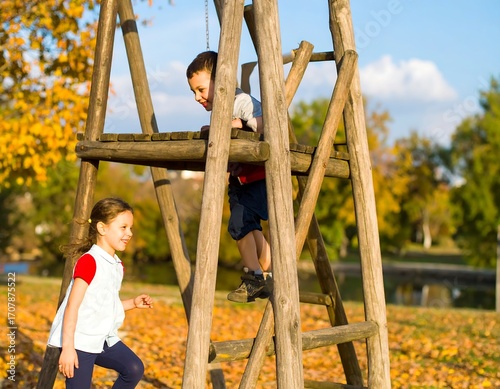 Two children playing on a wooden play structure in a park