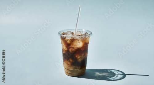 Iced coffee in a clear plastic cup with a flat lid and straw on a pastel blue background, minimal studio composition with soft halo shadow