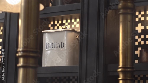Vintage metal bread box with rustic design placed on a kitchen shelf. Warm lighting and dark cabinetry create a cozy, nostalgic kitchen atmosphere. Interior kitchen design. 
