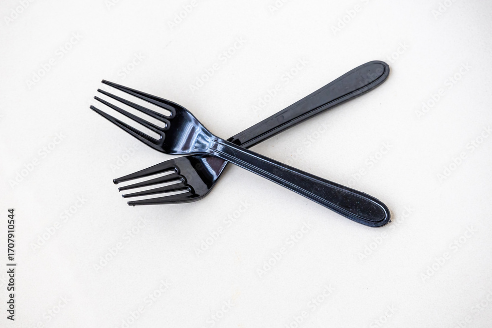 Fototapeta premium Two black plastic forks, isolated on a white background. These disposable utensils are a global environmental concern, contributing to plastic pollution and landfill waste.