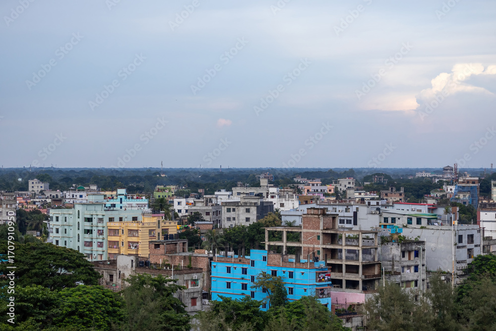 Fototapeta premium Scenic Kishoreganj, Bangladesh cityscape with modern high-rise buildings and verdant trees under an expansive afternoon sky. A perfect blend of urban development and nature.