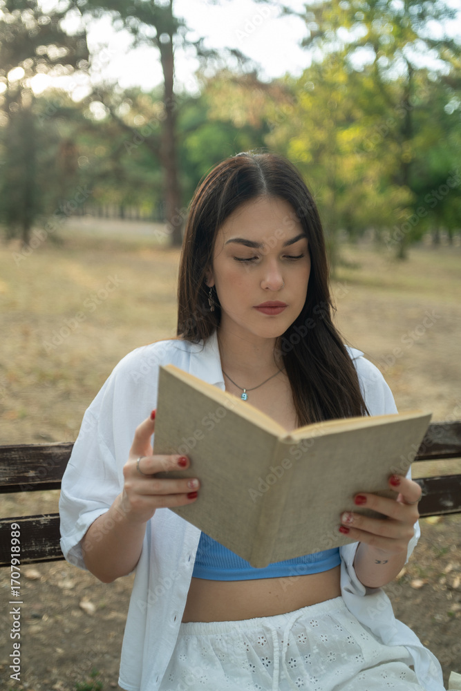 Fototapeta premium A young woman reading a book in the park, a female student learning from a book outdoors
