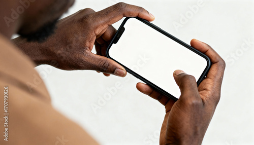 African man hands holding smartphone with a blank white screen for mockup. Mobile phone display for app or website design. Over the shoulder view of a person using the device.