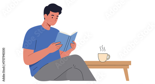 A young man sits comfortably on the floor reading a book, with a steaming cup of coffee on a small wooden table next to him.