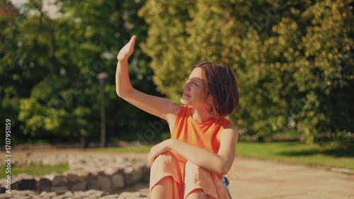 Sunshine enjoyment and playfulness: young girl shielding sun with palm in park
