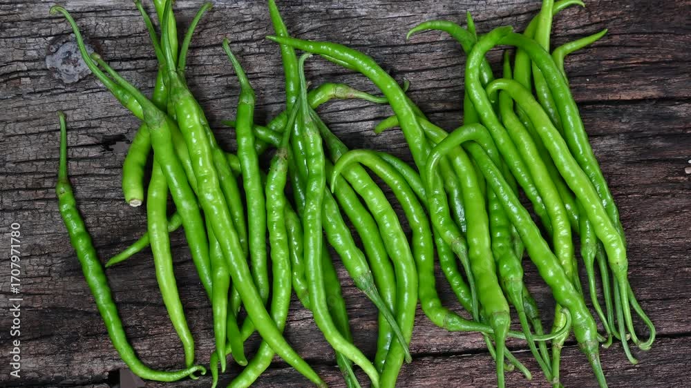 Close-up of fresh organic green chili peppers placed in a wooden bowl on a rustic wooden table. Healthy spicy vegetable used as a cooking ingredient in Indian and Asian cuisine.