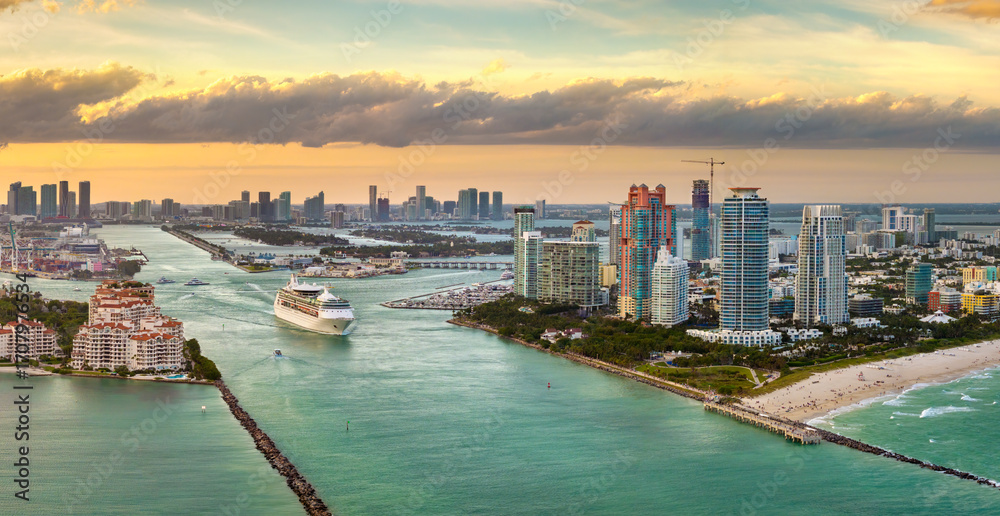 Obraz premium Luxurious cruise ocean liner sailing at Miami port harbor through main channel near South Beach. Hotels and residential buildings on waterfront and high skyscraper towers of downtown in distance