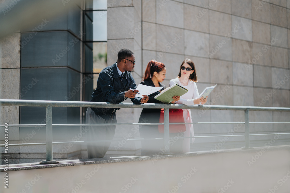 Fototapeta premium Three professionals engage in a conversation over documents while standing outside near a contemporary office building.