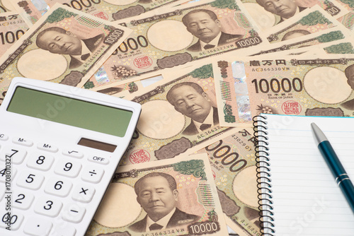多数の一万円札上に置かれた電卓とノートとペン