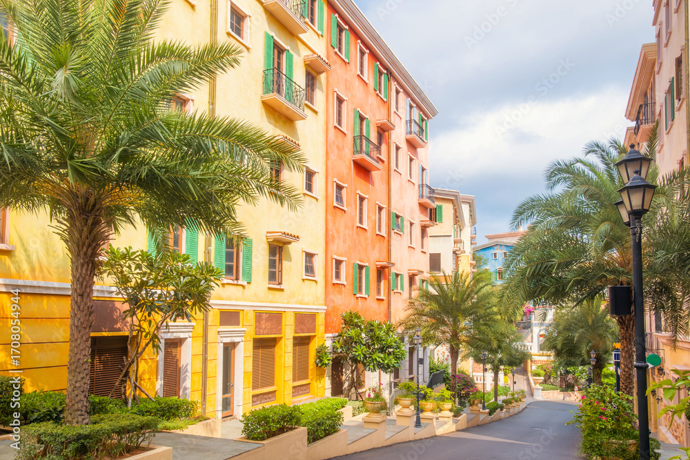 Fototapeta premium Colorful Mediterranean style buildings with palm trees lining charming street in Sunset Town, Phu Quoc island, Vietnam. Italian architecture in Asia. Travel and touristic destination in Asia