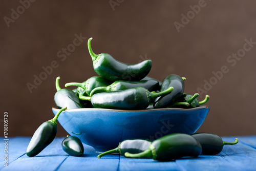 Blue ceramic bowl filled with green mexican jalapeno hot peppers on blue wooden table. Food photography