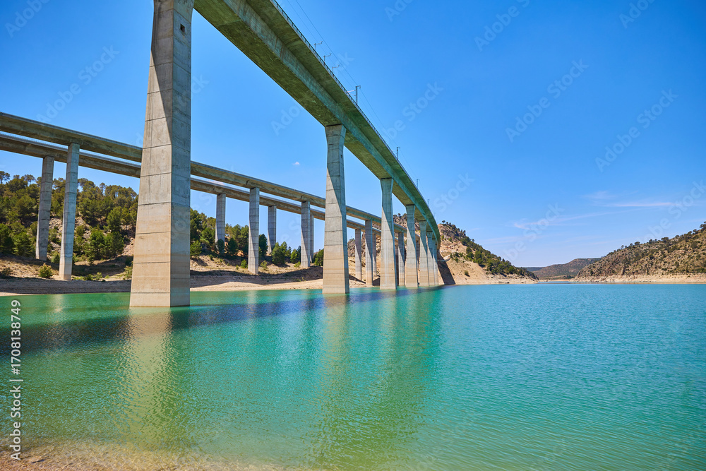 Fototapeta premium Tranquil scenery under a bridge over a reservoir with crystal clear turquoise water