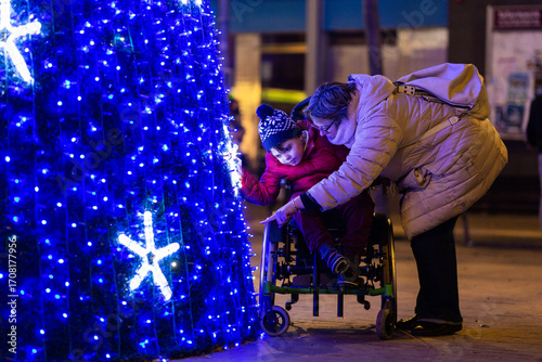Caring mother showing christmas tree lights to disabled son in wheelchair