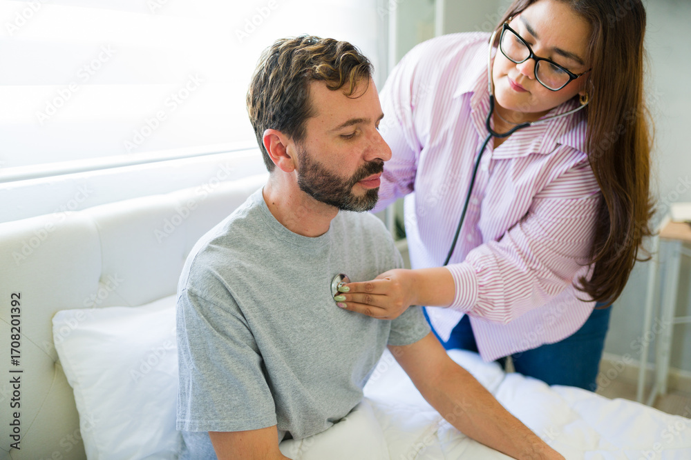 Fototapeta premium Female doctor examining patient with stethoscope at home after surgery
