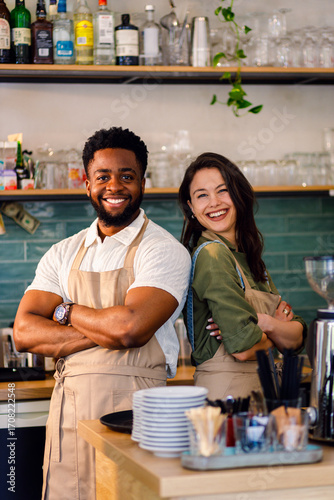 Portrait of male and female barista standing in her coffee shop behind the counter looking at camera.