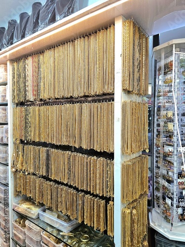 retail display, likely in a jewelry or accessories store. The main focus is a large collection of necklaces, predominantly gold-toned, hanging neatly on multiple horiz