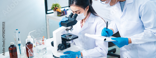 Team of scientists collaborating in a laboratory, with a female researcher using a microscope and a colleague recording notes, symbolizing teamwork, healthcare diagnostics, and innovation.