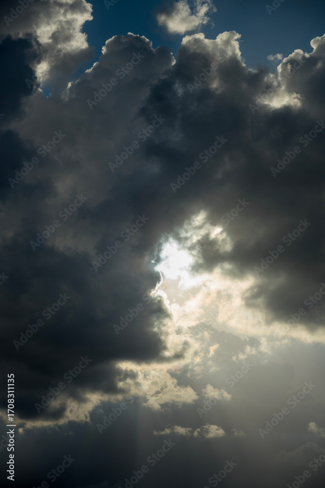 Obraz premium Dramatic sky with powerful sun rays breaking through dark storm clouds, creating an ethereal and atmospheric scene.