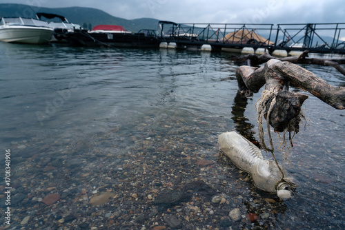 Fototapeta Naklejka Na Ścianę i Meble -  Plastic bottle pollution in lake water near dock, symbol of environmental problem and water contamination.