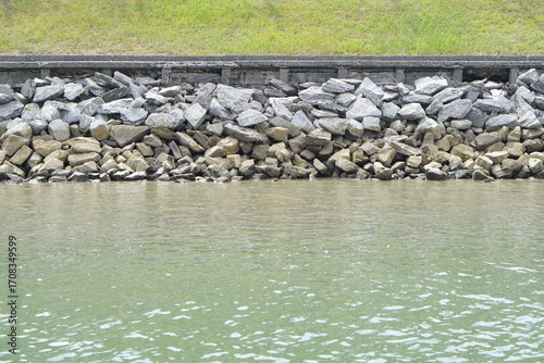 Riprap shoreline with stacked stones and calm green water along an embankment, erosion control structure forming rugged texture and pattern, natural waterfront background
