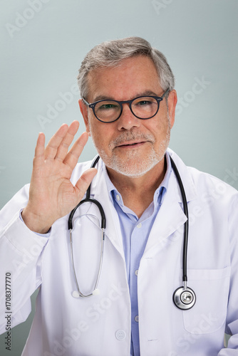 A doctor in a white coat smiles and waves, ready for an online consultation. He has a stethoscope around his neck and appears welcoming, emphasizing the convenience of virtual health care.