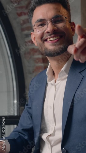 Hindu happy business man businessman with laptop in office pointing hey you gesture at camera smiling positive satisfied choosing with index finger joyful Arabian male manager executive guy working