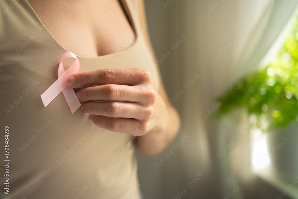 Obraz premium Close-up shot of female hand touching pink breast cancer awareness ribbon on shirt, symbolizing medical support and solidarity in October.