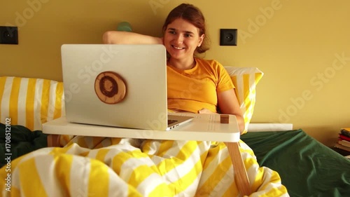 A Woman Happy Surprise. Good News on a Laptop in Bed. A Cozy Morning with Good News. A Woman with a Laptop and Yellow Bedding. Digital Happiness. A Woman Reading Good News on Her Laptop in Bed