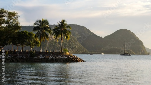 A waterfront with coconut palms and mountains in the background
