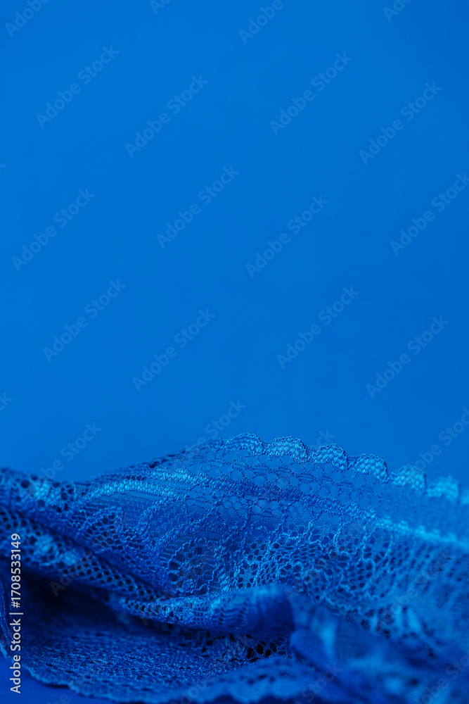 Obraz premium Blue lace fabric on blue background with copy space, vertical. High quality photo