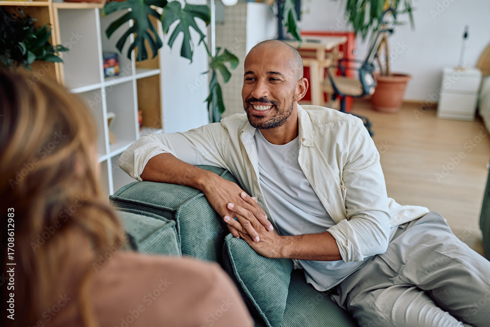 Fototapeta premium Happy man talking with his psychologist during therapy session while sitting on comfortable sofa in cozy living room