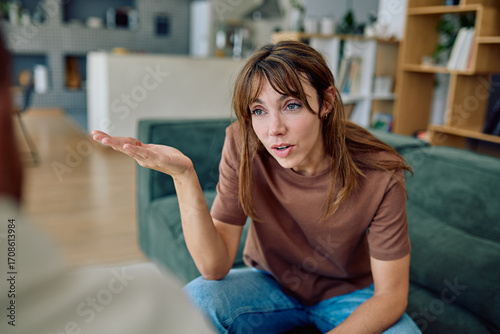 Young woman sitting on sofa is gesturing while explaining something to her psychotherapist during therapy session