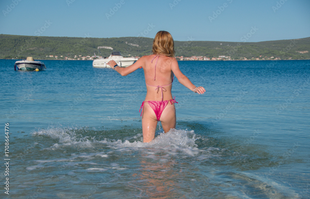 Naklejka premium attractive woman in pink bikini runs into water on beach in croatia