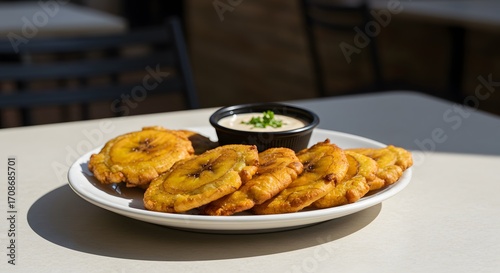A plate of golden patacones served with a creamy dipping sauce garnished with green onions on top