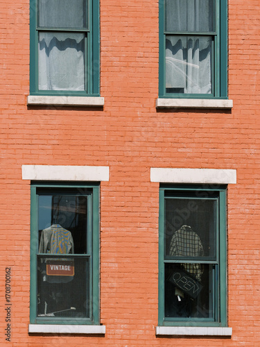 Vintage clothing displayed in windows of a red brick building in a bustling urban area