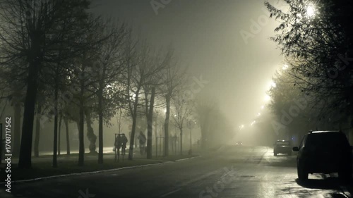 People pedestrians walk along a dark gloomy deserted city street at night in fog with poor visibility