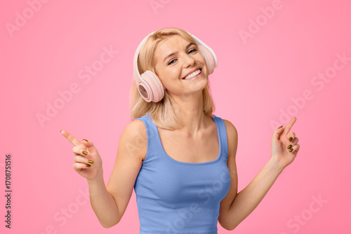 Fotografie Carefree woman in headphones dacing to her favorite music and smiling on yellow studio background