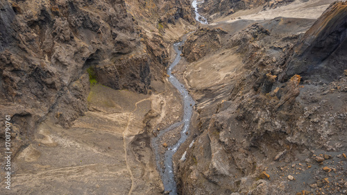 Narrow canyon with steep rocky cliffs and a winding river cutting through the barren volcanic landscape of Iceland